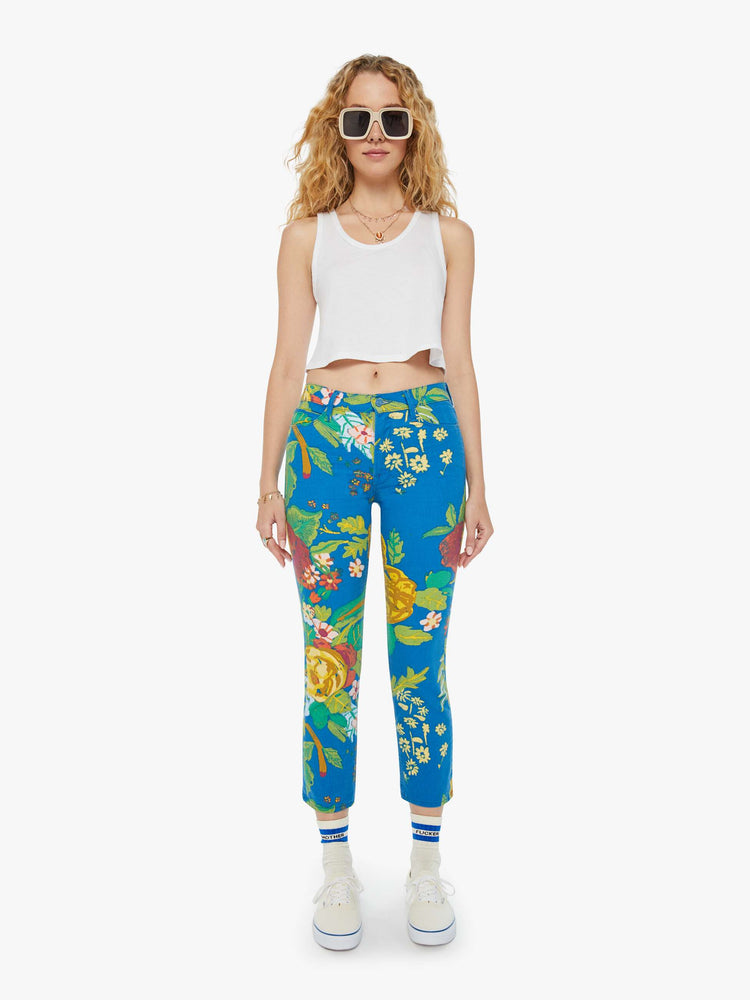 Front view of a woman in bright blue tropical floral print straight leg jeans with a cropped hem and styled with a white tank top. 