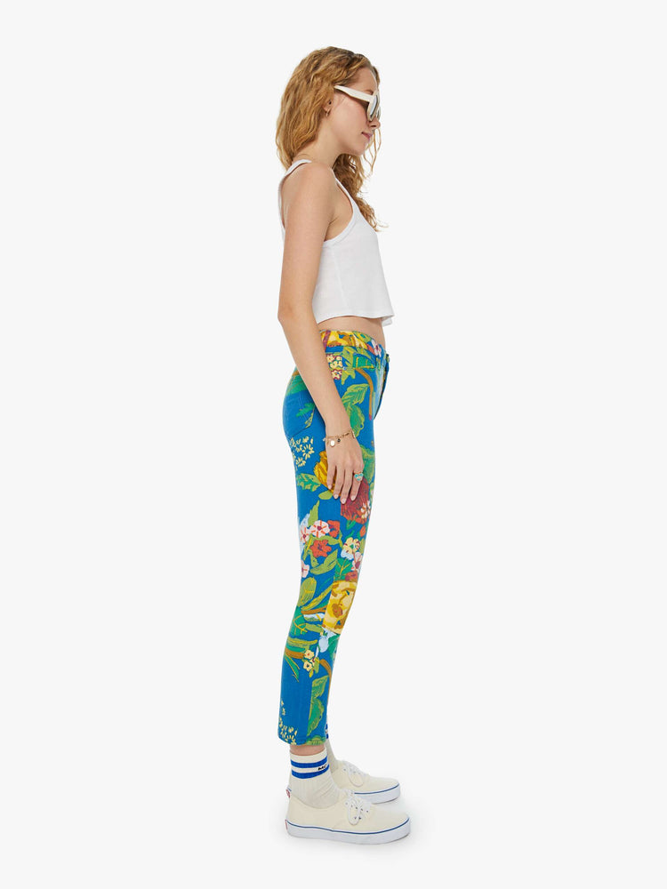 Side view of a woman in bright blue tropical floral print straight leg jeans with a cropped hem and styled with a white tank top. 