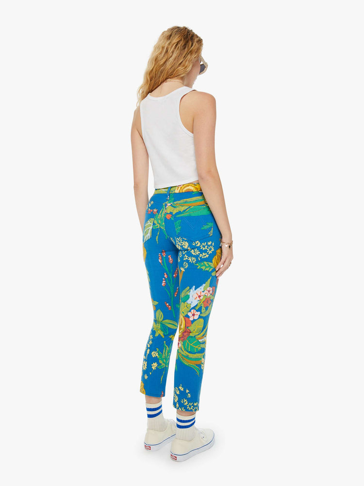 Back view of a woman in bright blue tropical floral print straight leg jeans with a cropped hem and styled with a white tank top. 