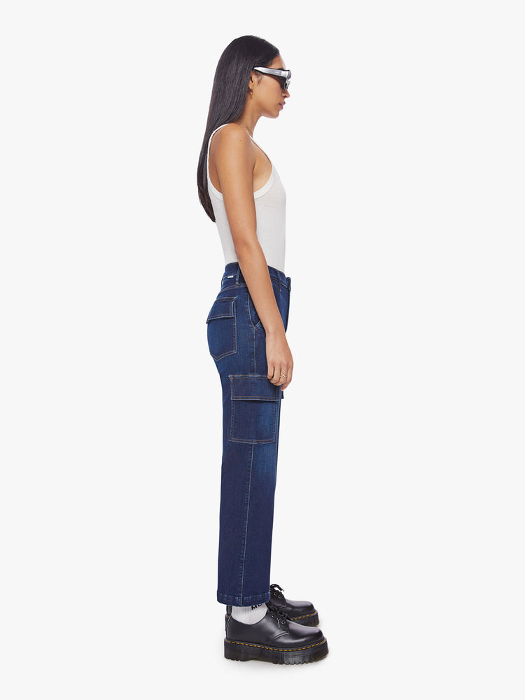 Side view of a woman dark blue wash high-waisted ankle-length pants with a wide straight leg, cargo pockets and seams down the front.