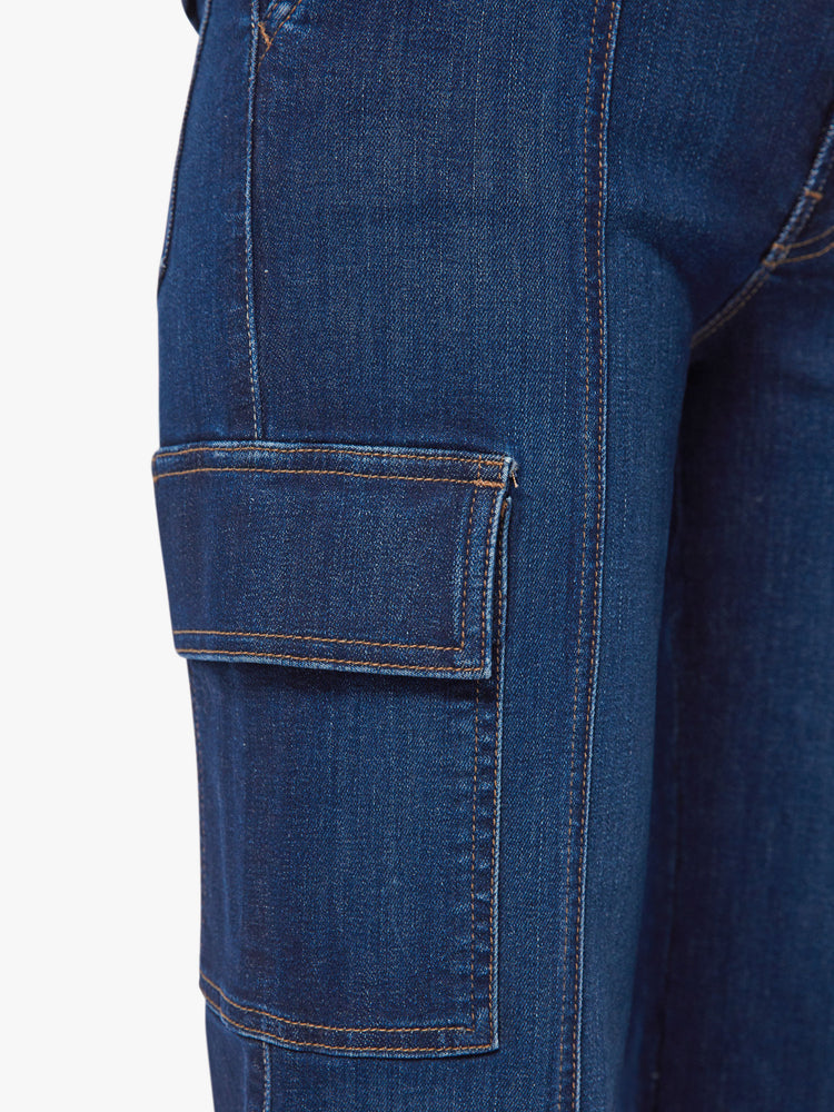 Pocket close up view of a woman dark blue wash high-waisted ankle-length pants with a wide straight leg, cargo pockets and seams down the front.
