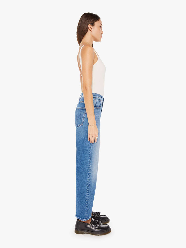 Side view of a woman igh-waisted jeans with a loose wide leg and an ankle-length inseam in a medium blue wash.