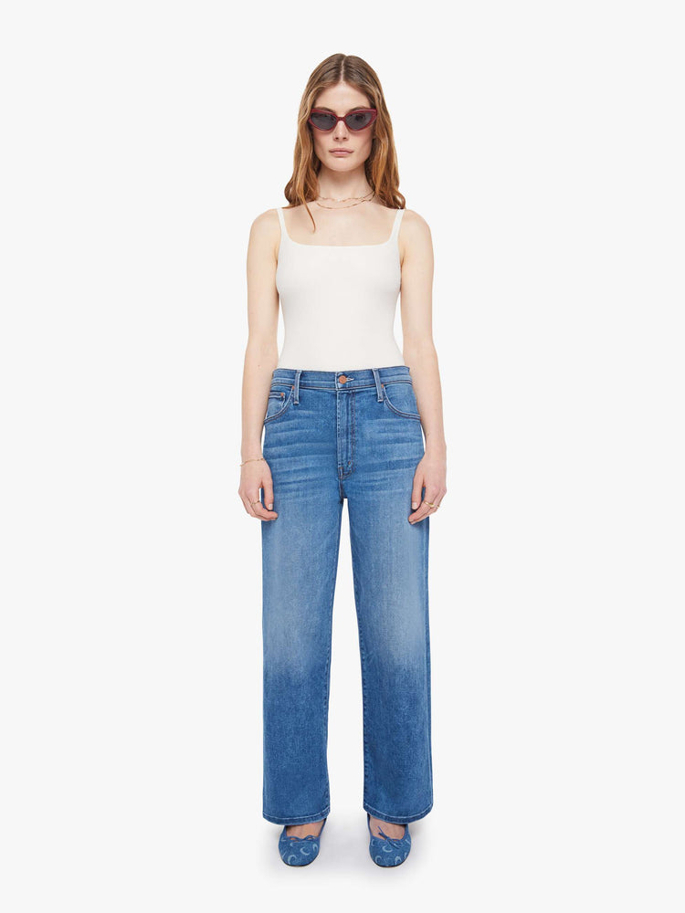 Front view of a woman in a mid blue jean that sit lower on the hips with a zip fly, loose wide leg and a clean ankle-length inseam.