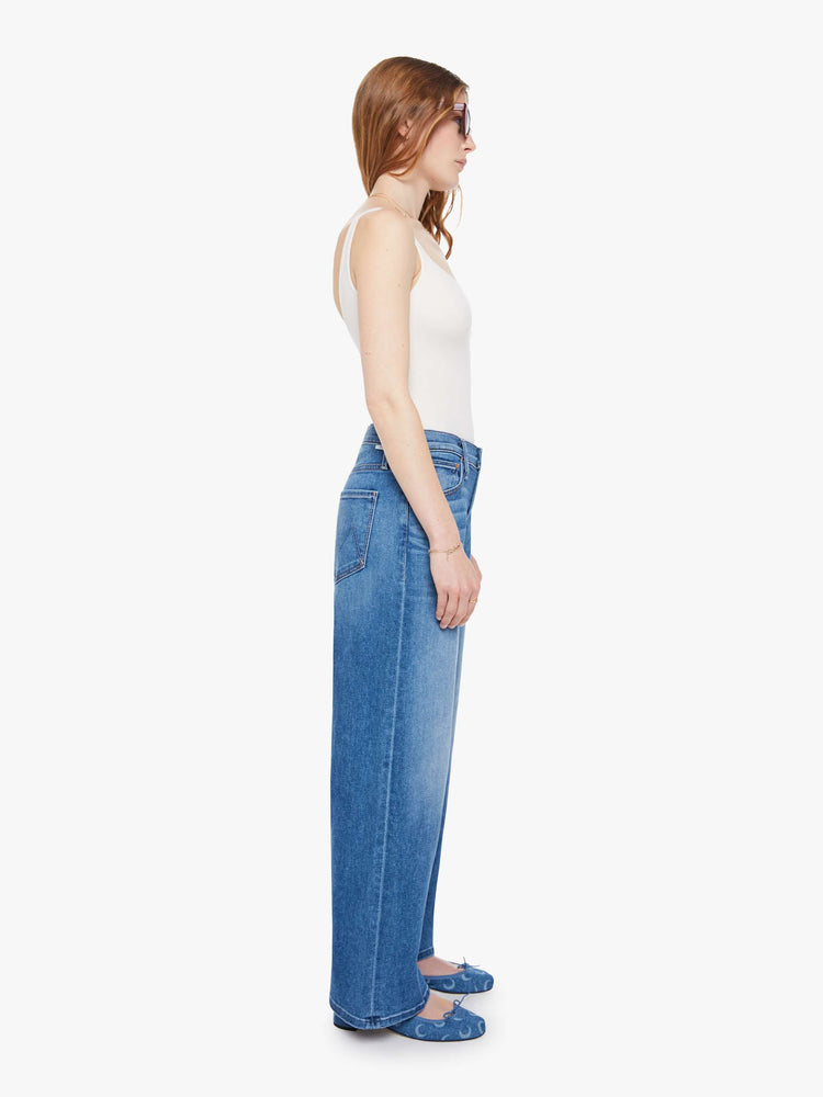 Side view of a woman in a mid blue jean that sit lower on the hips with a zip fly, loose wide leg and a clean ankle-length inseam.