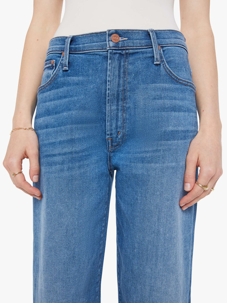 Close up view of a woman in a mid blue jean that sit lower on the hips with a zip fly, loose wide leg and a clean ankle-length inseam.