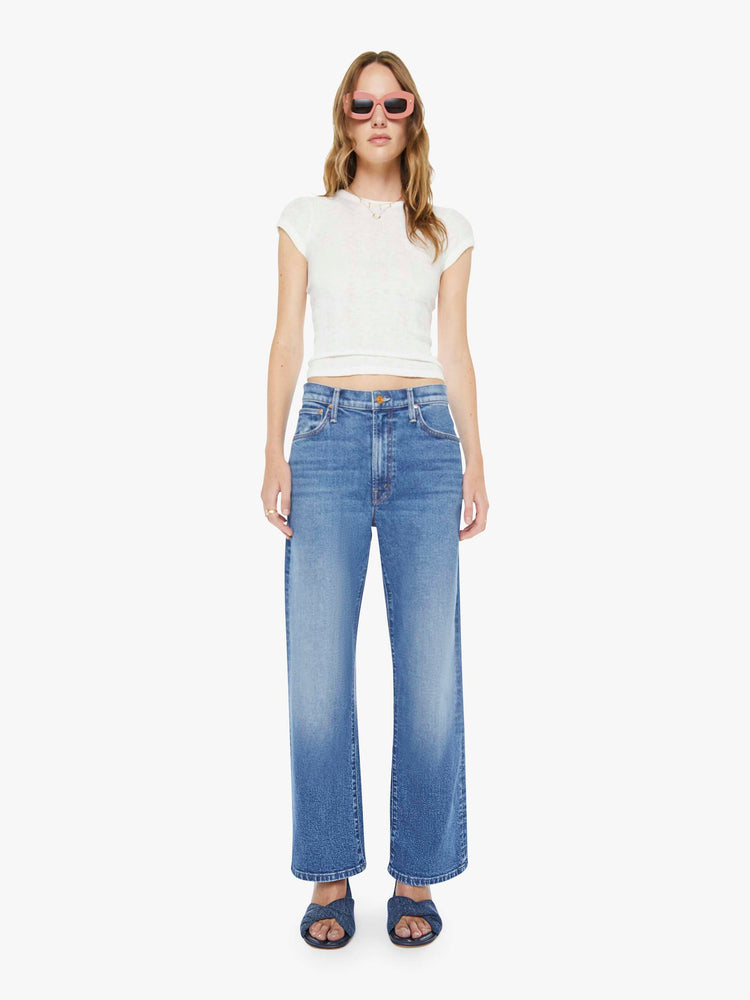 Front view of a woman in a mid blue jeans designed to sit lower on the hips with a zip fly, loose wide leg and a clean ankle-length inseam. 