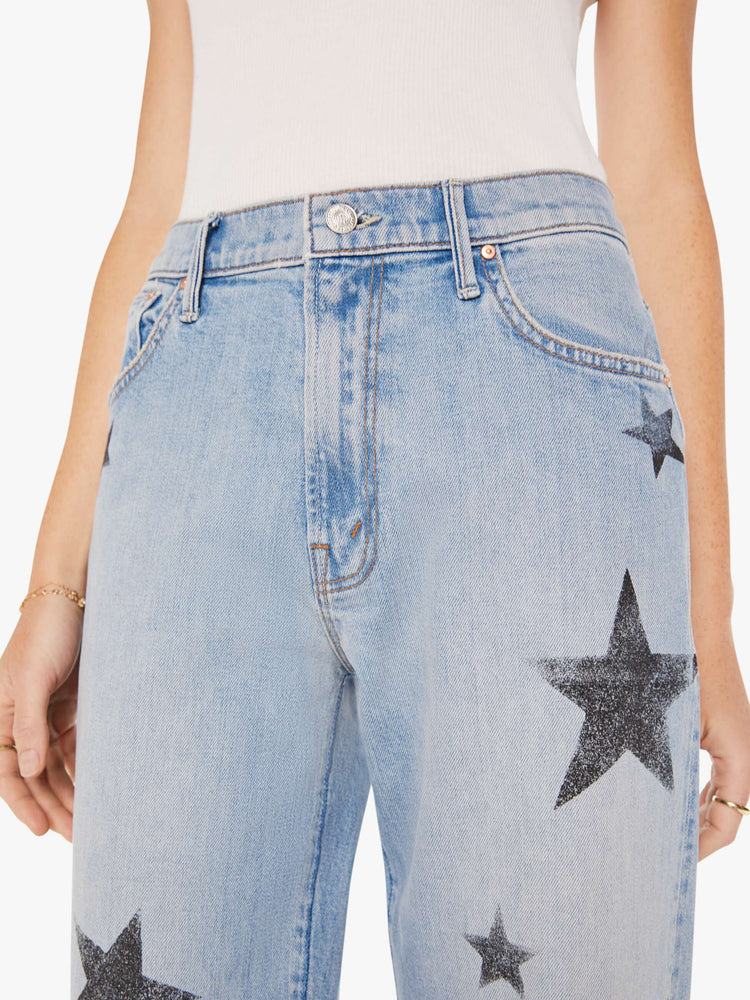 Waist close up view of a woman in a light blue with faded stars through out jean with high-waisted jeans with a loose straight leg and an ankle-length inseam with a clean hem.