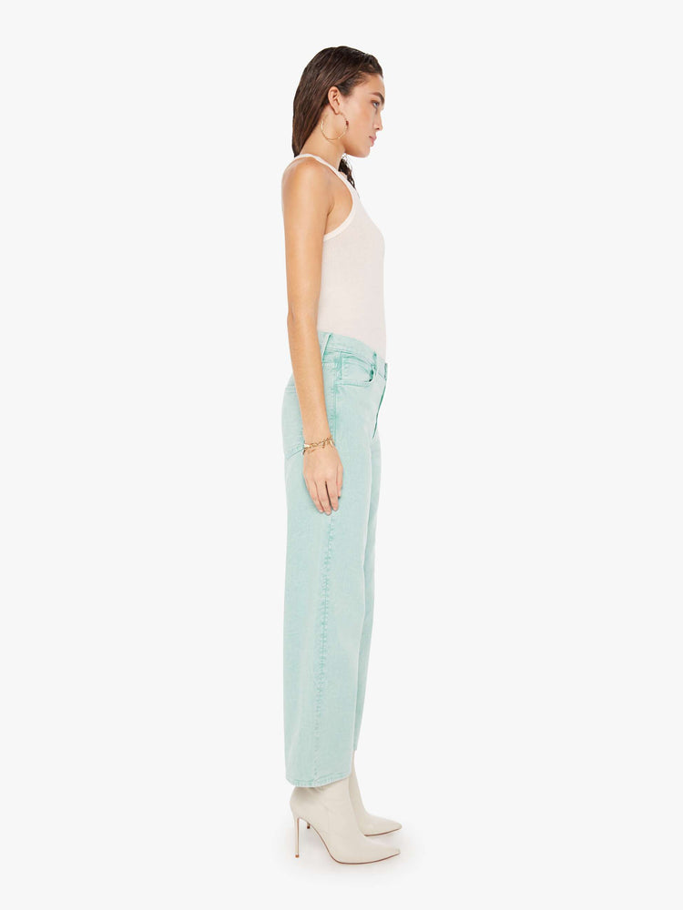Side view of a woman wearing a light teal acid wash pant featuring a wide leg and ankle length hem.
