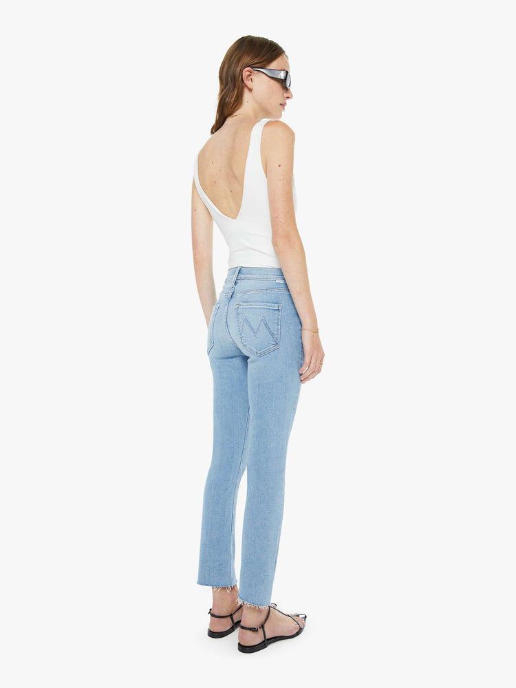 Back view of a woman in a med blue mid-rise straight leg hits at the ankle with a frayed hem.