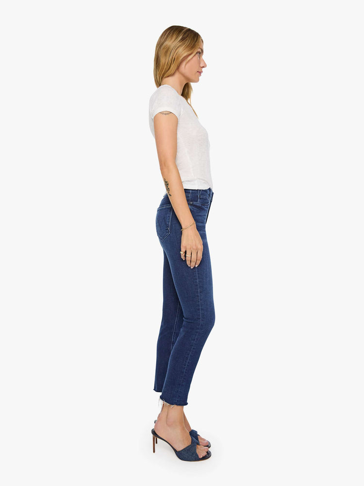 Side view of a woman in a dark blue  mid-rise straight leg jean that hits at the ankle with a frayed hem. 