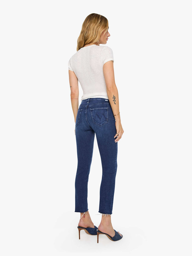 Back view of a woman in a dark blue  mid-rise straight leg jean that hits at the ankle with a frayed hem. 