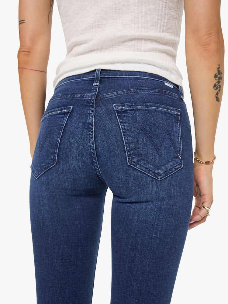 Close up view of a woman in a dark blue  mid-rise straight leg jean that hits at the ankle with a frayed hem. 