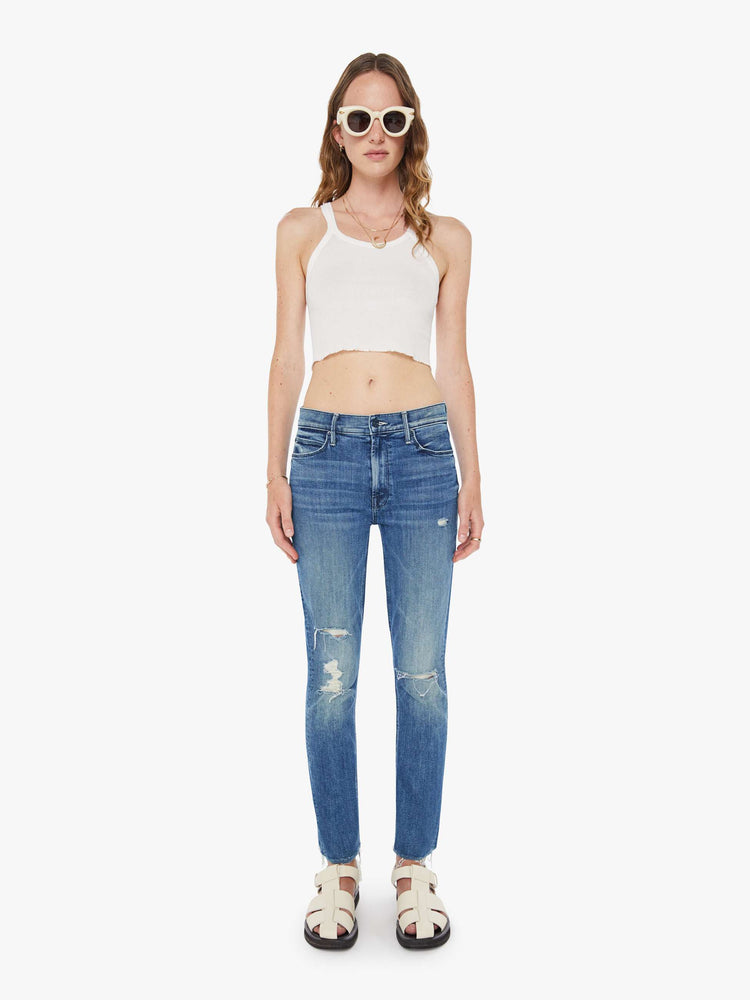 Front view of a woman in a mid blue mid-rise jeans with a straight leg, ankle-length inseam and a frayed hem.