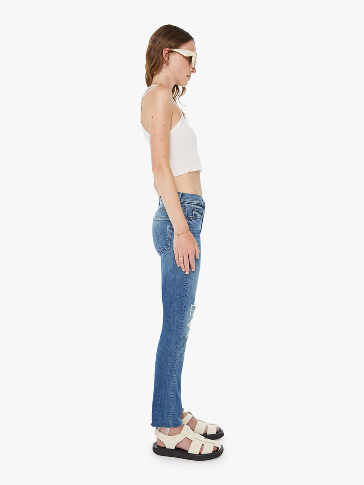 Side view of a woman in a mid blue mid-rise jeans with a straight leg, ankle-length inseam and a frayed hem.
