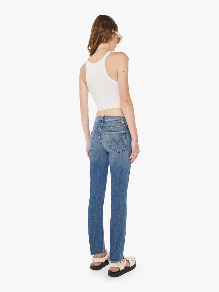 Back view of a woman in a mid blue mid-rise jeans with a straight leg, ankle-length inseam and a frayed hem.