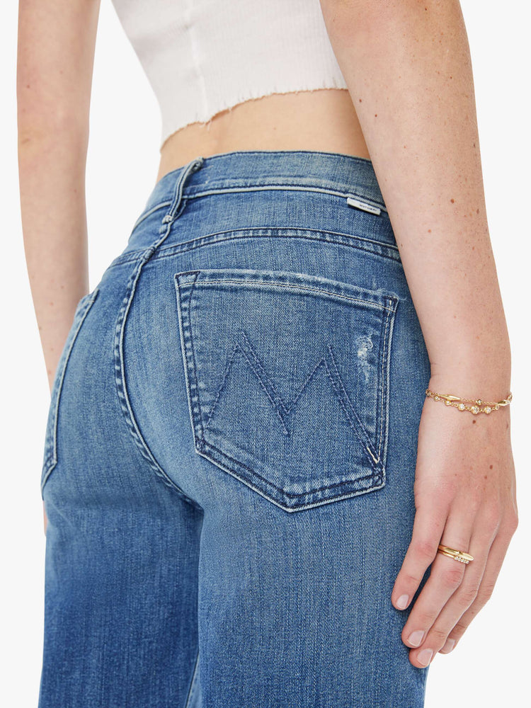 Back close up view of a woman in a mid blue mid-rise jeans with a straight leg, ankle-length inseam and a frayed hem.