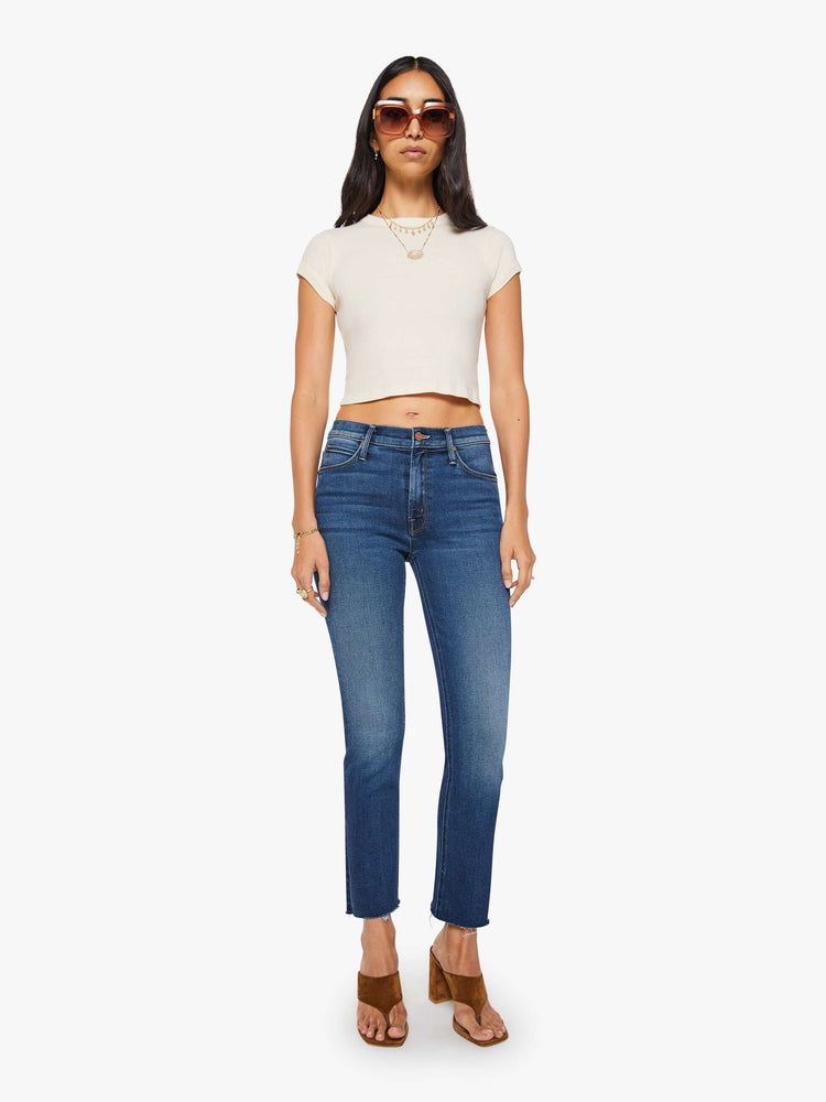 Front view of a woman in  dark blue mid-rise straight leg hits at the ankle with a frayed hem.