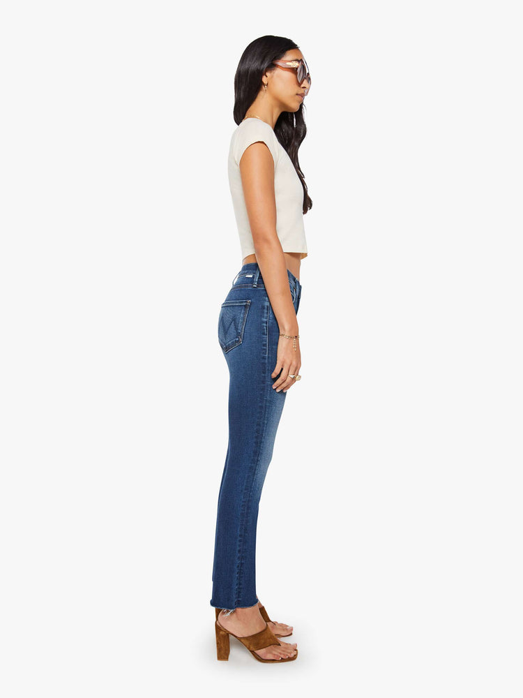 Side view of a woman in  dark blue mid-rise straight leg hits at the ankle with a frayed hem.