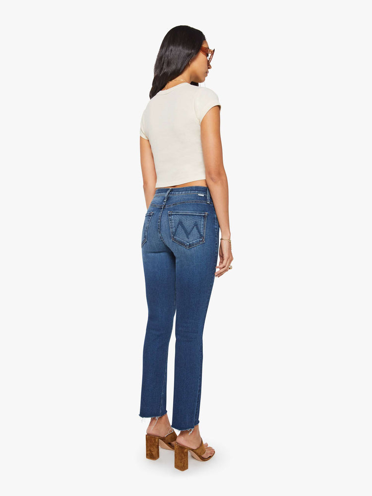 Back view of a woman in  dark blue mid-rise straight leg hits at the ankle with a frayed hem.