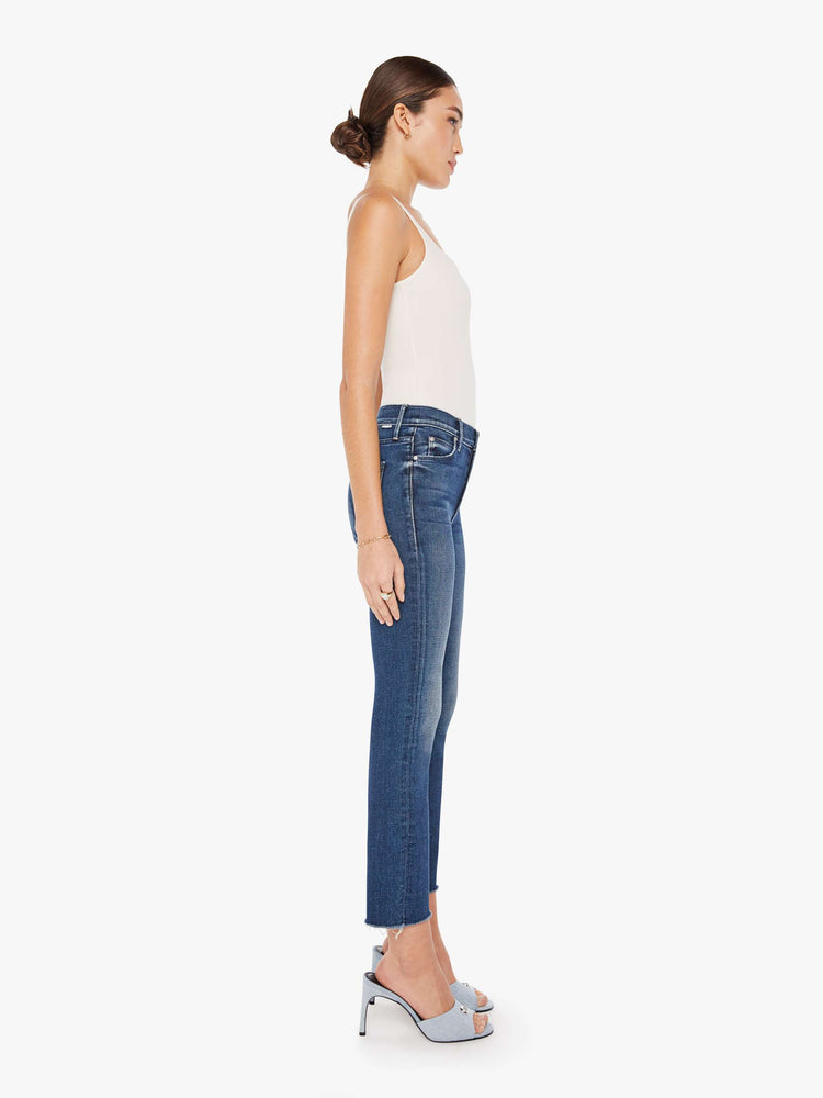 Side view of a womens dark blue wash jean featuring a mid rise, skinny leg, and an ankle length frayed hem.