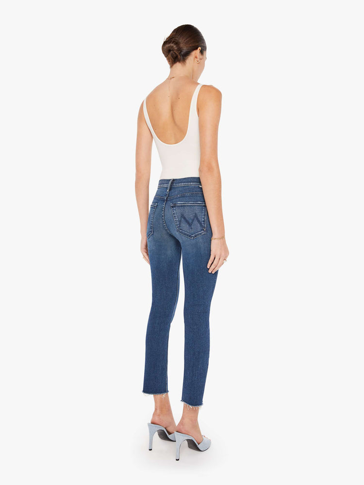 Back view of a womens dark blue wash jean featuring a mid rise, skinny leg, and an ankle length frayed hem.