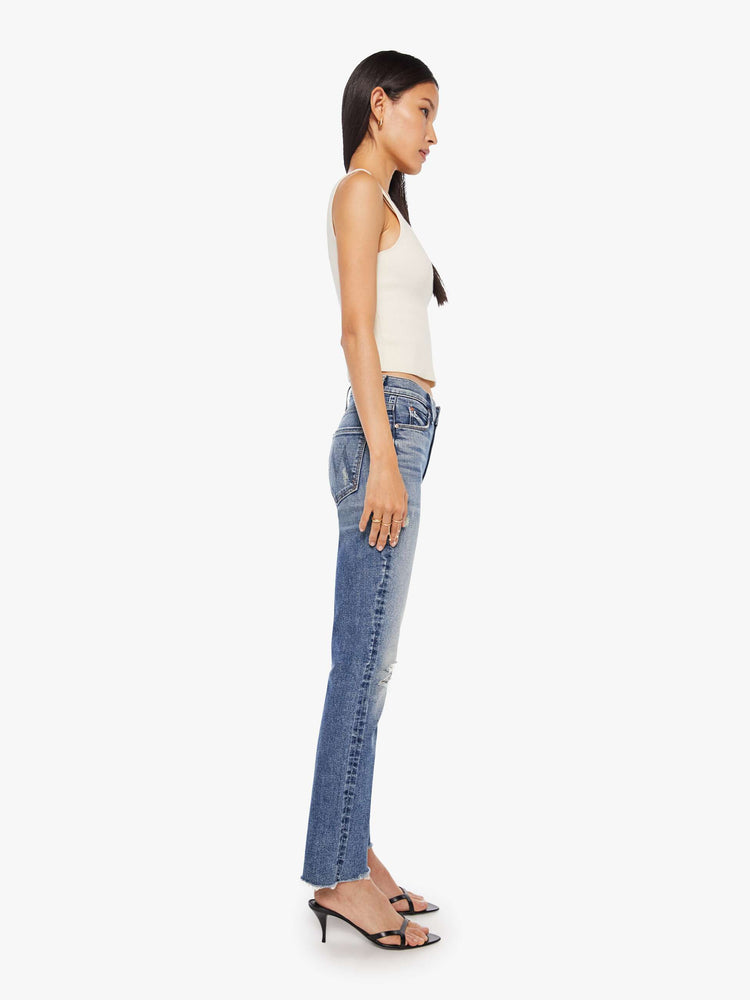 Side  view of a women's medium blue mid-rise jean with a slim straight fit and a frayed ankle length hem.