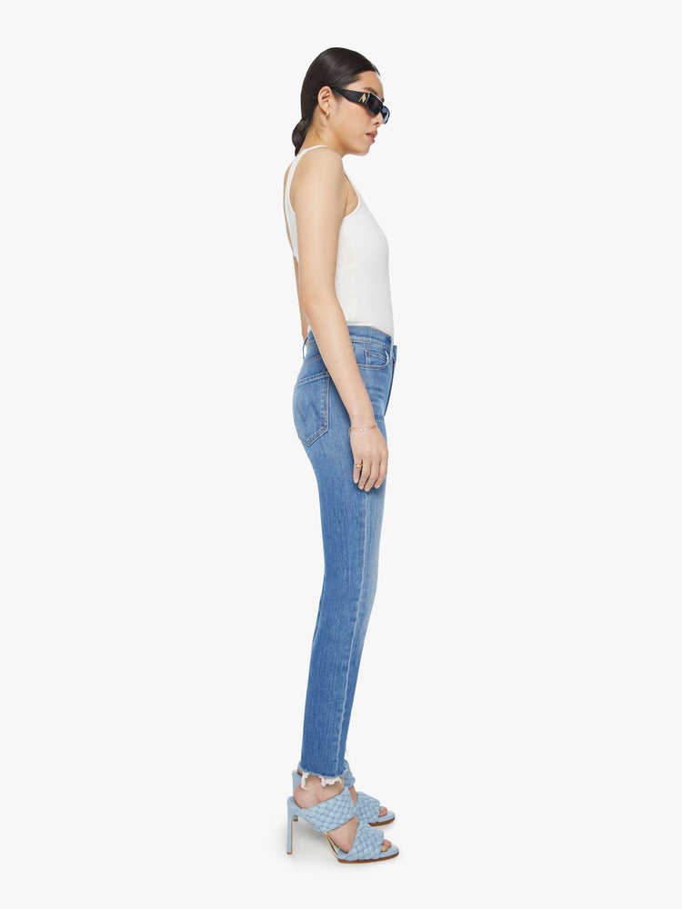 Side view of a woman mid-rise straight leg with an ankle-length inseam and a frayed hem in a mid-blue wash.