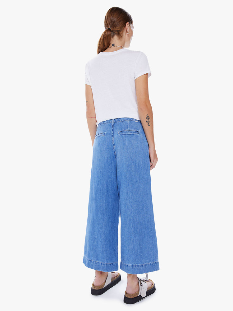 Back view of a women high-waisted wide-leg pants with an ankle-length inseam and pleats at the waist in a mid-blue wash with faded details.