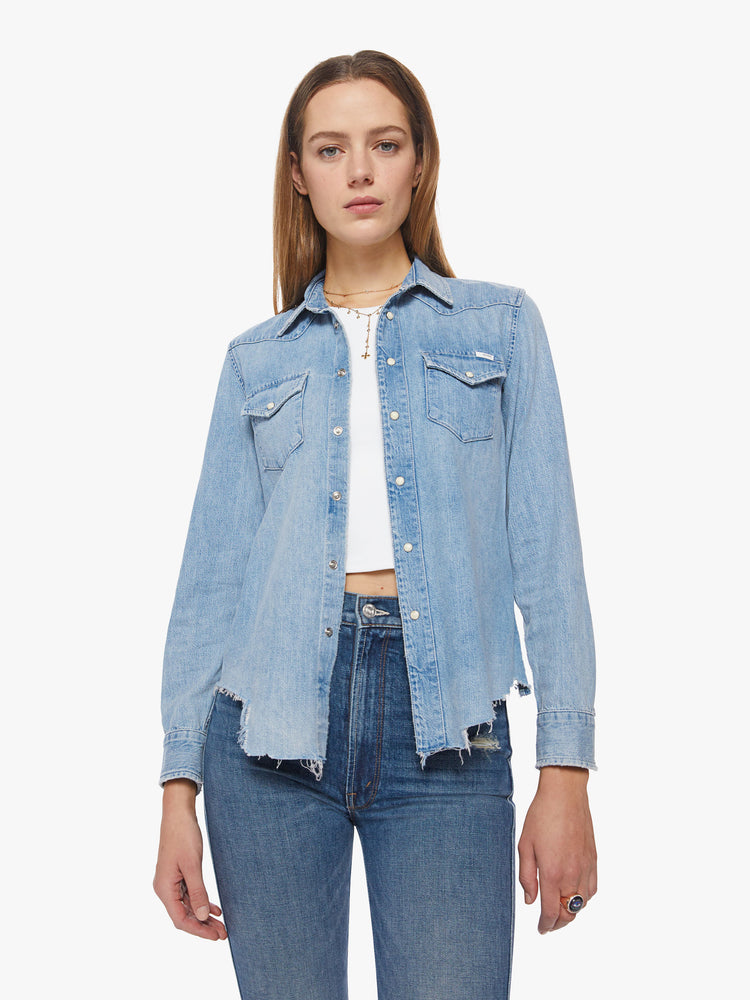 Front view of a woman denim button-up with front patch pockets and a raw, uneven hem in a light blue wash.