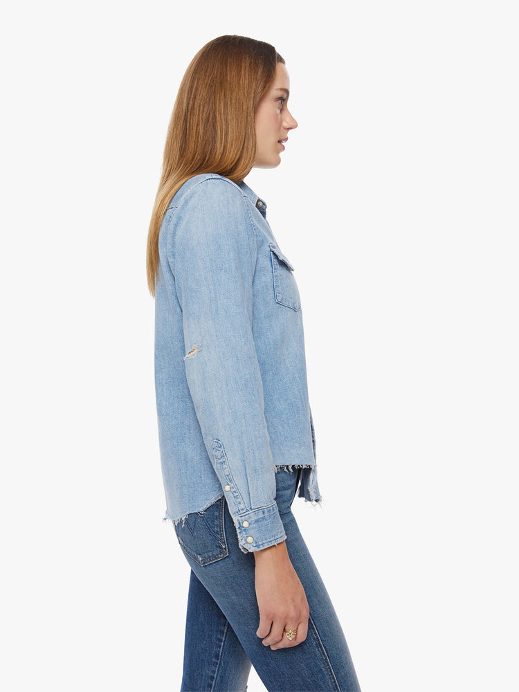 Side view of a woman denim button-up with front patch pockets and a raw, uneven hem in a light blue wash.