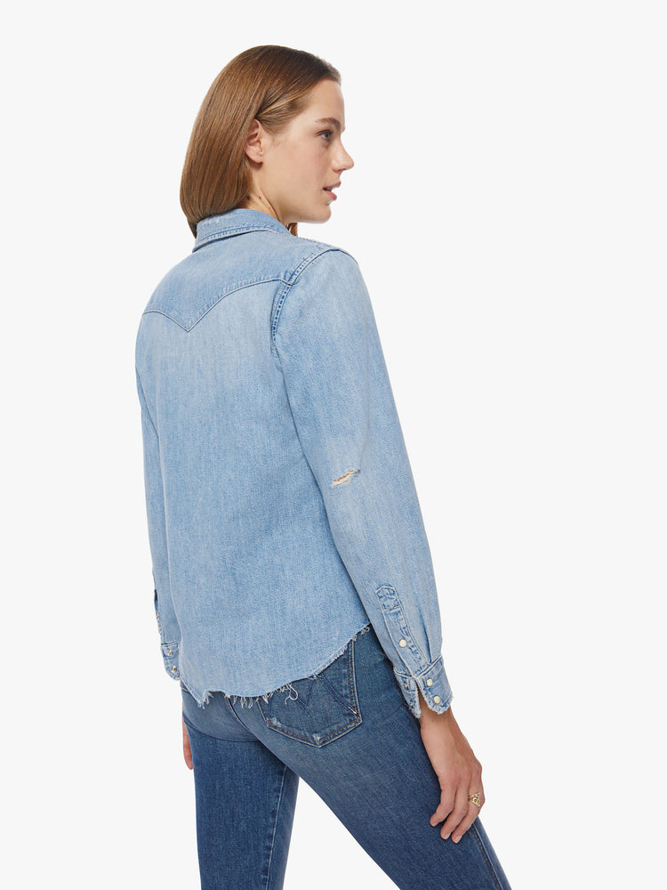 Back view of a woman denim button-up with front patch pockets and a raw, uneven hem in a light blue wash.