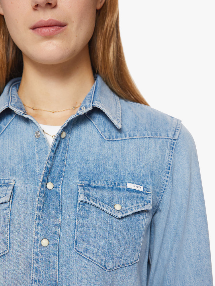 Close up button view of a woman denim button-up with front patch pockets and a raw, uneven hem in a light blue wash.
