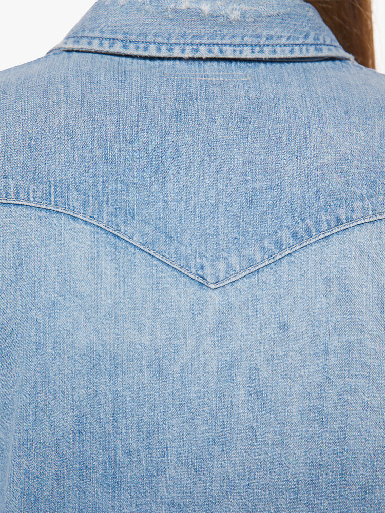 Back view of a woman denim button-up with front patch pockets and a raw, uneven hem in a light blue wash.