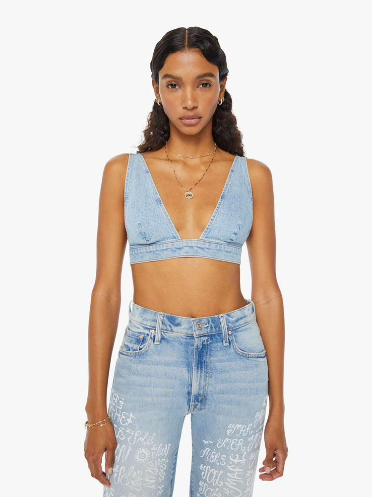 Front view of a woman in a light blue denim bralette with a deep V-neck, thick underband, adjustable straps and a button closure in the back.