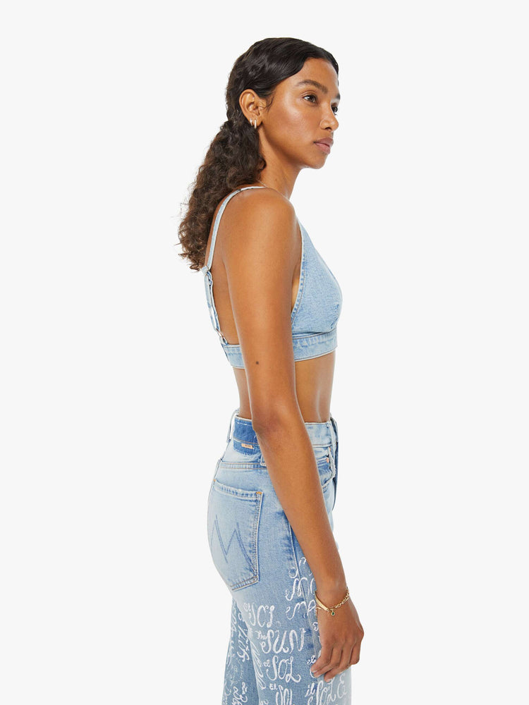 Side view of a woman in a light blue denim bralette with a deep V-neck, thick underband, adjustable straps and a button closure in the back.
