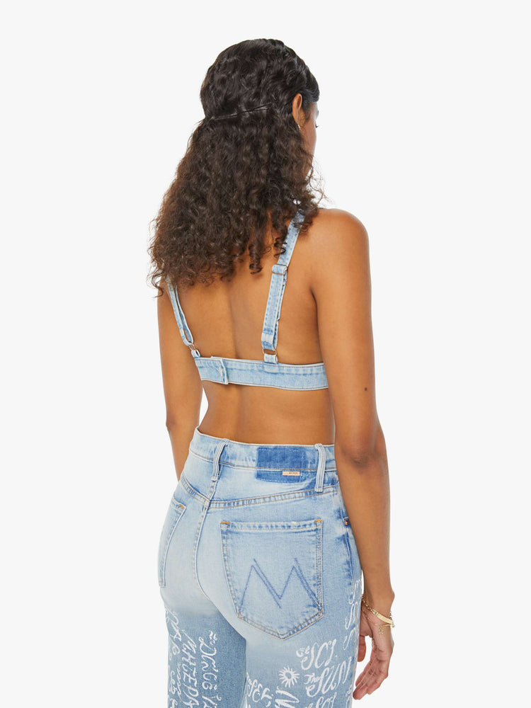 Back view of a woman in a light blue denim bralette with a deep V-neck, thick underband, adjustable straps and a button closure in the back.