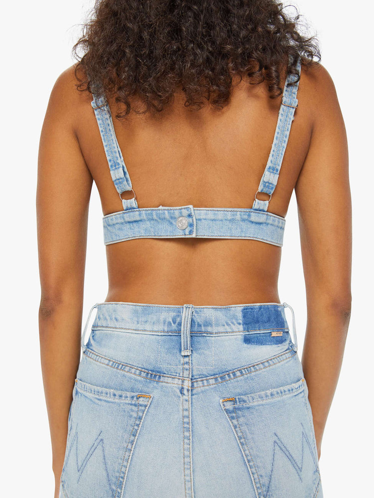 Detailed view of a woman in a light blue denim bralette with a deep V-neck, thick underband, adjustable straps and a button closure in the back.