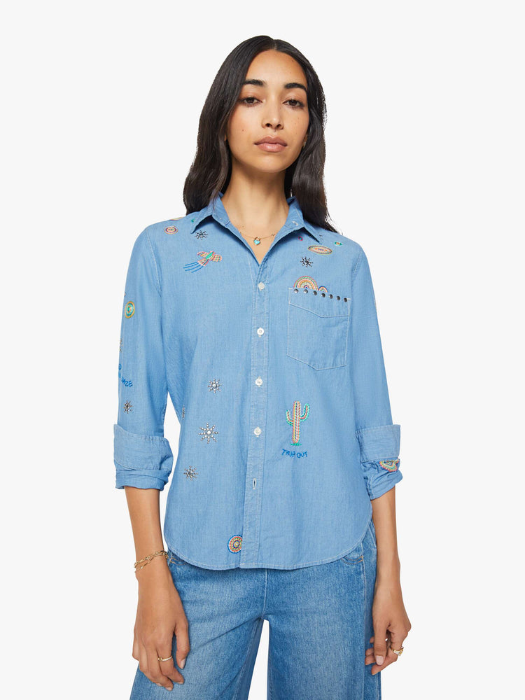 Front view of woman in a blue with colorful embroidery button-up blouse with patch pockets and a curved hem.