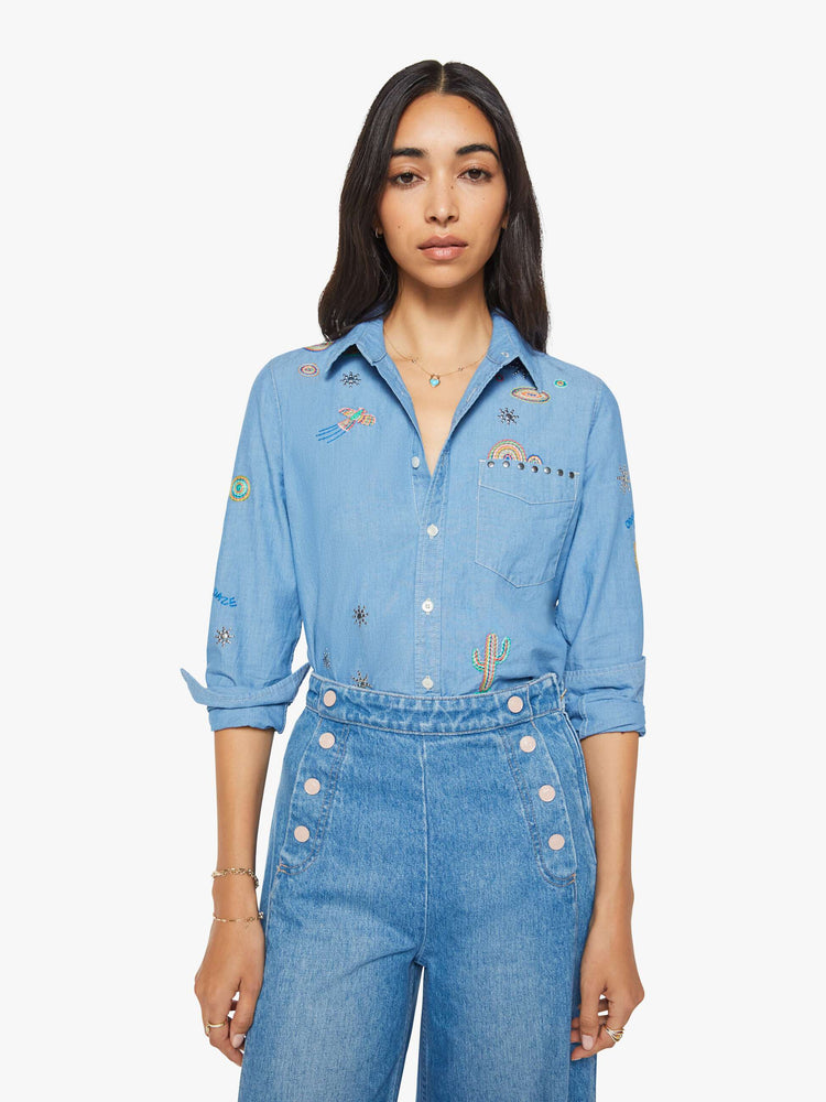 Front view of woman in a blue with colorful embroidery button-up blouse with patch pockets and a curved hem.