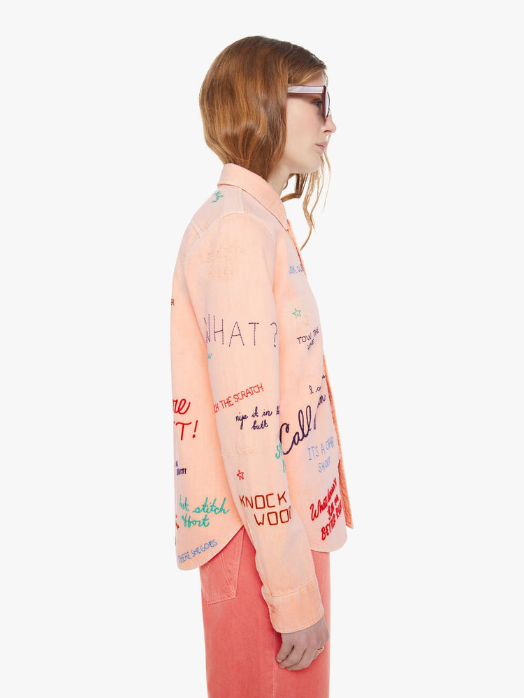 Side view of a woman in a faded orange with embroidery button-up blouse with patch pockets and a curved hem.