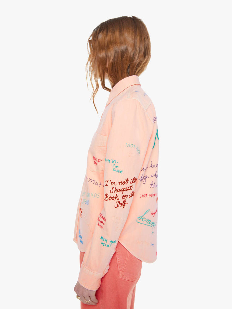 Side view of a woman in a faded orange with embroidery button-up blouse with patch pockets and a curved hem.