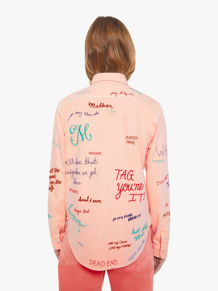 Back view of a woman in a faded orange with embroidery button-up blouse with patch pockets and a curved hem.