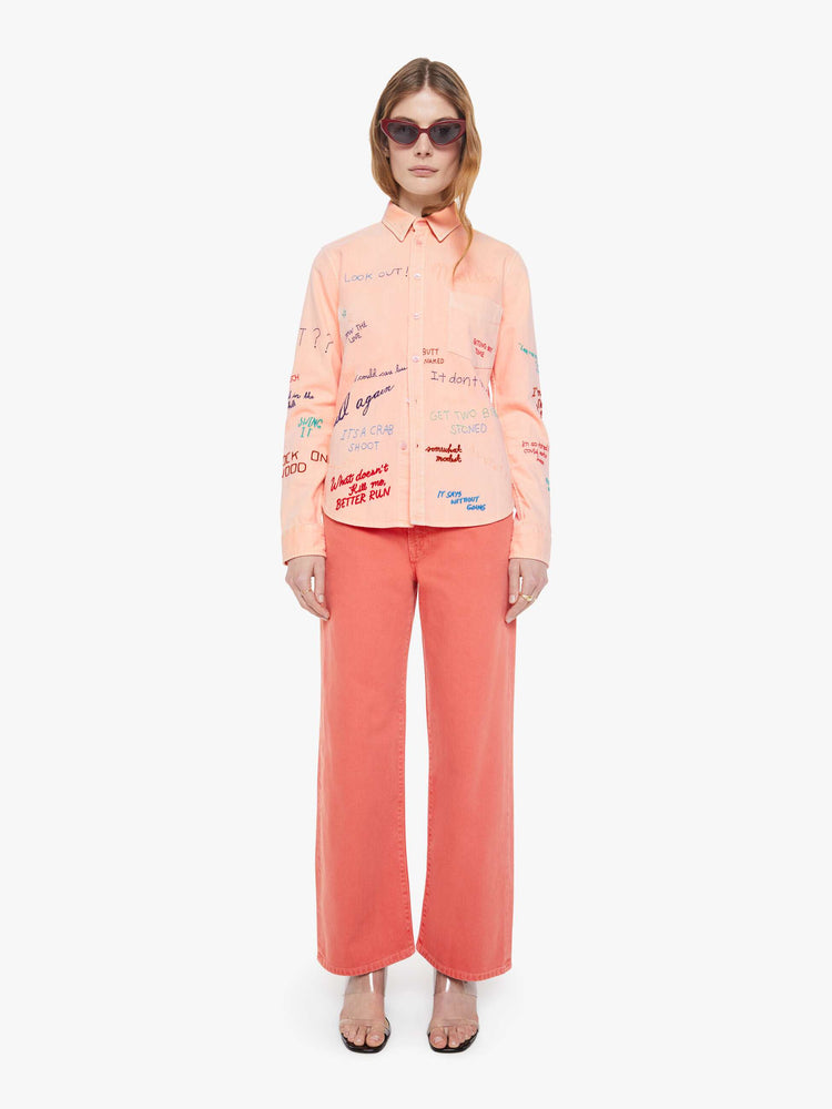 Front view of a woman in a faded orange with embroidery button-up blouse with patch pockets and a curved hem.