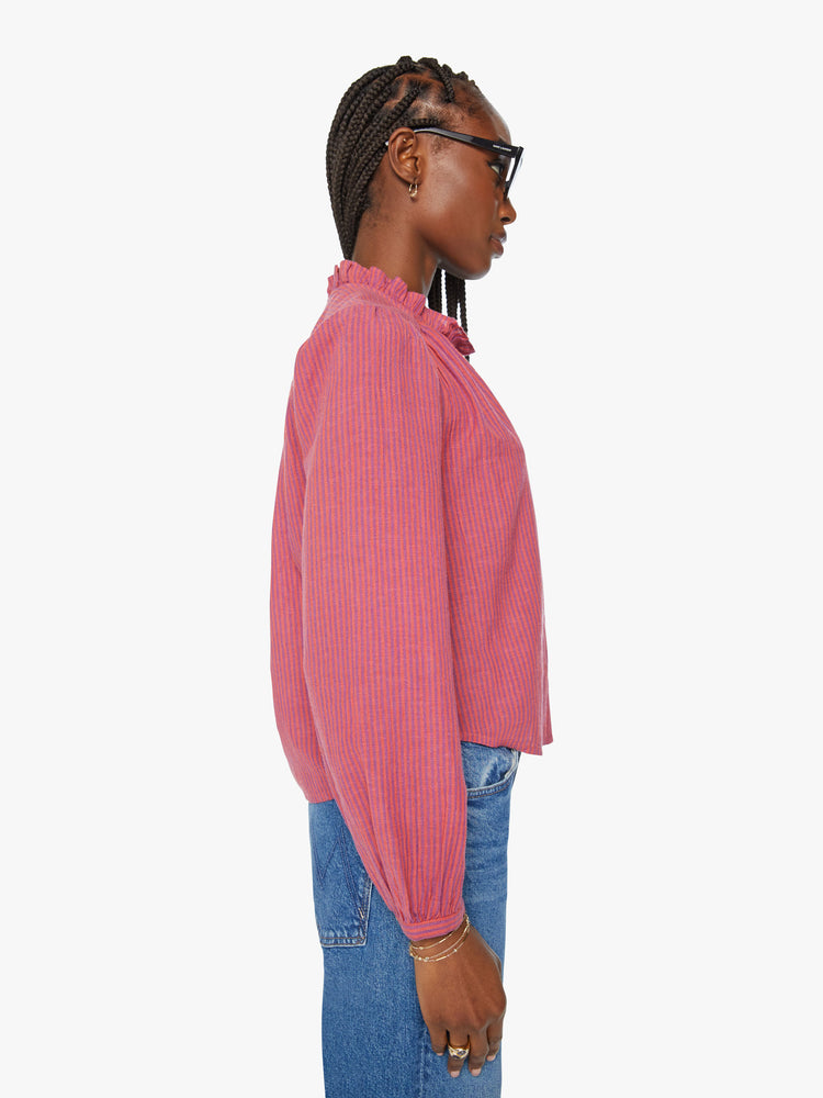 Side view of a woman salmon with light purple stripes crewneck blouse with a ruffled collar, puffed shoulders, long balloon sleeves and buttons down the front.