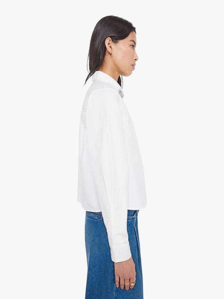 Side view of a woman in a white twist on the classic button-up with long sleeves, a hidden button panel and a cropped fit.
