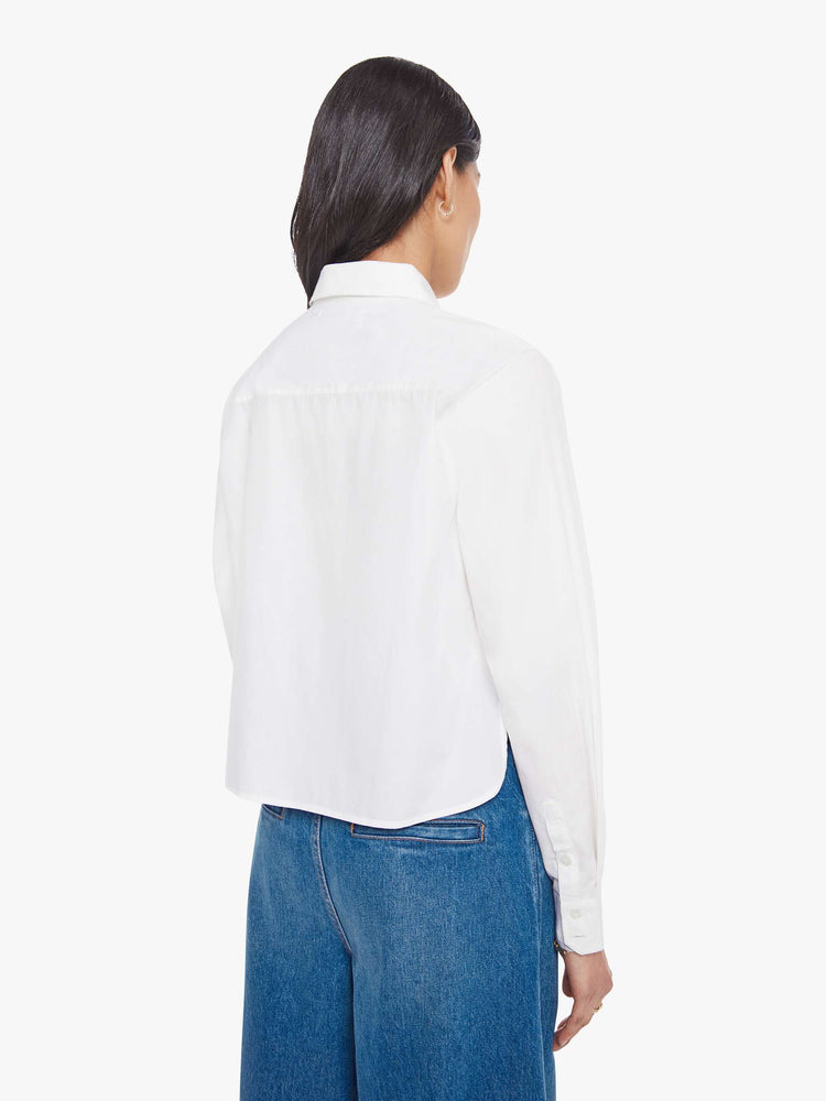 Back view of a woman in a white twist on the classic button-up with long sleeves, a hidden button panel and a cropped fit.