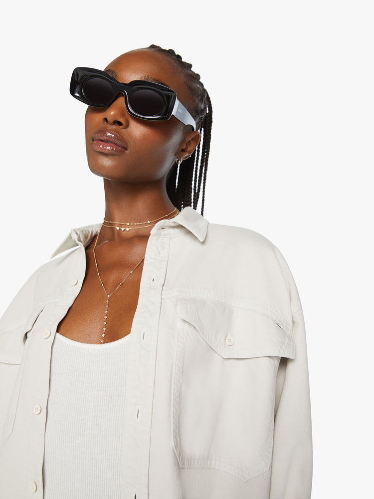 Close up view of a woman oversized button-up with drop shoulders, patch pockets and a curved hem in an off white hue.