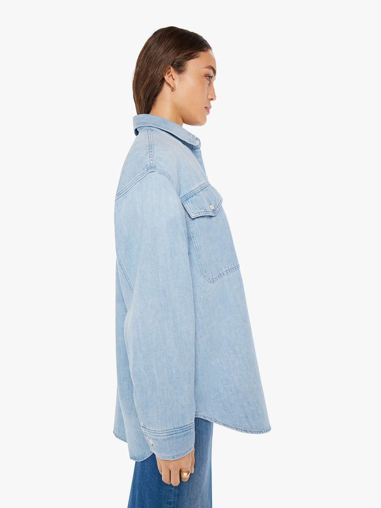 Side view of a woman oversized button-up with drop shoulders, patch pockets and a curved hem in a light blue wash with white buttons.
