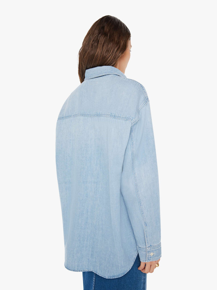 Back view of a woman oversized button-up with drop shoulders, patch pockets and a curved hem in a light blue wash with white buttons.