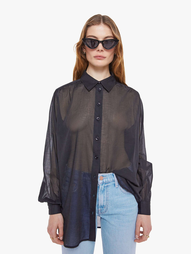 Front view of woman in a sheer black  collared button-up blouse with long balloon sleeves, a curved hem and an oversized fit. 